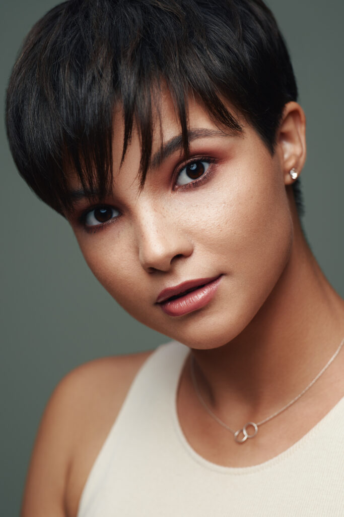 Femme aux cheveux courts avec une coupe pixie élégante, mise en valeur par un maquillage subtil et un style minimaliste.